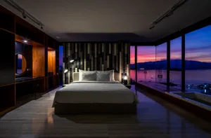 Modern minimalist bedroom with concrete and marble materials and a view of the sunset over the water.