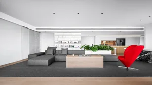 Modern minimalist living room with concrete accents featuring a grey sectional sofa, red chair, and green plant.