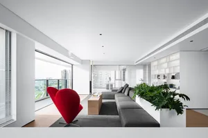Contemporary living room featuring grey fabric sofa, red accent chair, large windows, and indoor green plant.