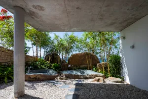 A sleek concrete outdoor bathroom with natural stone features and lush greenery.