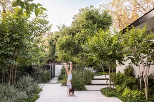 A person performing a handstand on a concrete pathway surrounded by lush greenery and plants in a modern outdoor garden setti