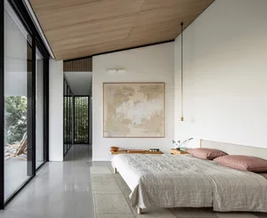 A minimalist bedroom featuring a modern wooden bed with pink pillows and a large abstract artwork on the wall.