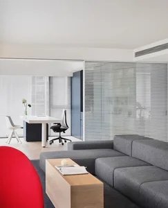 A modern living room featuring a grey sectional sofa, a red armchair, a wooden coffee table, and a white desk with a black ch