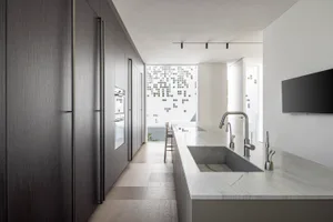 A modern minimalist kitchen featuring concrete and marble materials, with a white marble countertop and dark wooden cabinets.