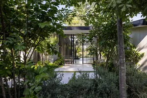 A modern residential entrance framed by greenery and metal gates, offering a serene and inviting atmosphere.