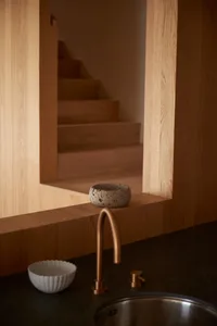 A minimalist kitchen with a wooden countertop, sink, and stone bowl on a wooden shelf.