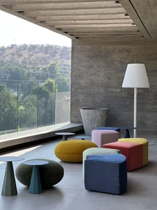 A modern indoor space featuring concrete walls and colorful textile ottomans and tables.