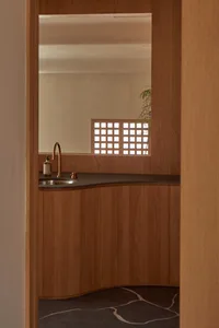 A modern kitchen interior with wooden cabinets, a black countertop, and a window with a latticed frame.