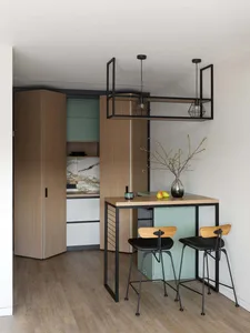A modern kitchen with wood and metal finishes, featuring a bar table with stools and a vase with pears on the table.