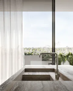 A modern kitchen with a marble countertop overlooks a serene outdoor garden.