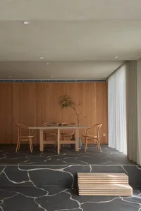 A modern minimalist dining room with wooden furniture and concrete floor. Includes lighting, wooden chairs, and a wooden tabl