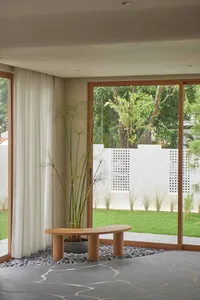 A minimalist living space featuring a stone floor, wooden bench, and glass window overlooking a green garden.