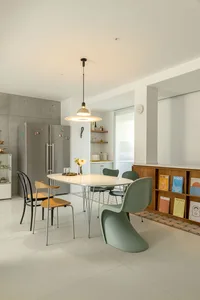 A modern, minimalist residential kitchen with white countertops, stainless steel appliances, wooden flooring, and a dining ta