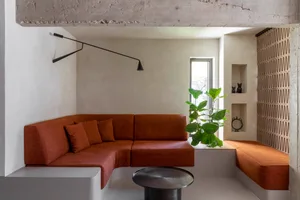 Modern living room with orange sectional sofa, concrete walls, and indoor plants.
