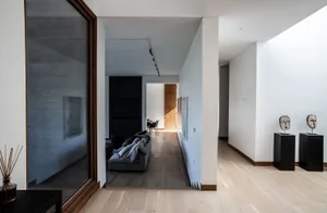 Modern minimalist living room featuring concrete walls, glass windows, and wood flooring.