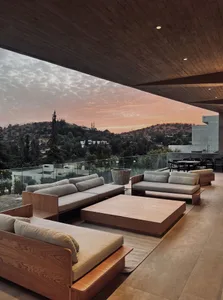 A modern minimalist outdoor living space featuring wooden furniture and a view of a sunset over a hillside.