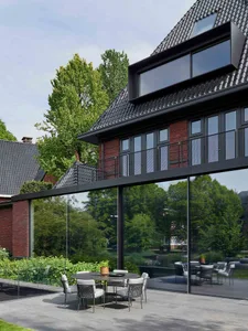 A modern house with a glass wall overlooking a green garden, featuring brick and metal materials.