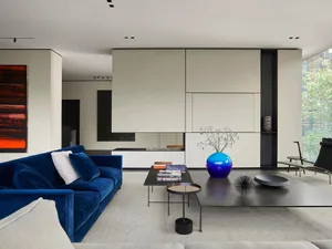 Modern minimalist living room with sleek blue sofa, black and white geometric coffee tables, and a blue vase with flowers.