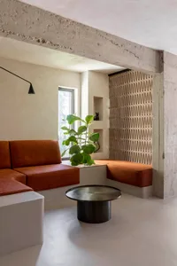 Modern living room with concrete walls and wooden seating, featuring a green plant on a white table and a concrete beam overh