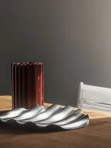 Three decorative metal objects with a wave-like, corrugated texture on a wooden table.