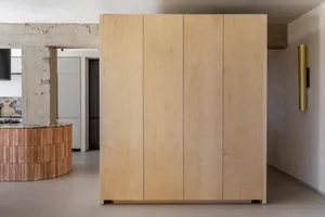A minimalist wardrobe cabinet made of light-colored wood, featuring four vertical panels.