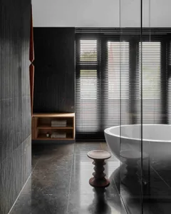 A modern bathroom featuring black granite flooring and walls with a freestanding bathtub and wooden stool with a minimalistic