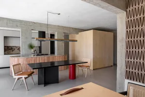 Modern dining room with concrete flooring, wooden table and chairs, and a metal pendant light hanging over the table.