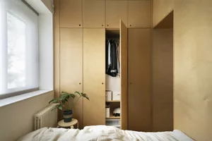 A minimalist bedroom featuring a wooden plywood storage system with an open closet.