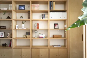 A minimalist bookshelf featuring wooden shelves and decorative objects including books, a lamp, and a clock.