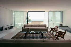 Modern minimalist living room featuring a comfortable beige couch, a coffee table with books, and a view of the ocean through