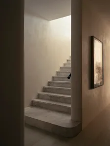 A minimalist staircase with marble steps and a white wall, illuminated by natural light from above.