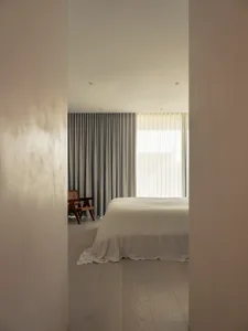 簡約臥室內擺放白色床鋪，窗戶上掛著灰色窗簾。