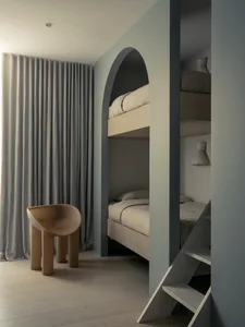Modern minimalist bedroom featuring wood bunk beds with gray curtains and a unique brown tube-shaped chair.