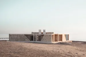 A minimalist concrete beach house with a modern, clean exterior featuring large glass windows and a simple, open floor plan.