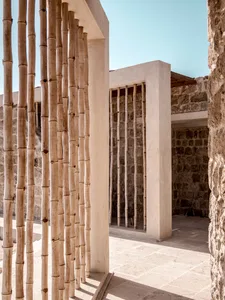 A modern architectural structure featuring tall wooden poles and stone walls.