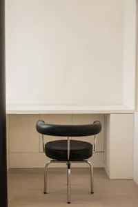 A modern, minimalist black leather chair with a round back and seat, placed in front of a sleek white desk.
