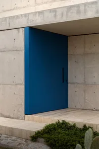 A modern entranceway with a large, blue door set into a concrete wall.