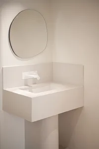 A modern minimalist bathroom with a white sink, concrete counter, and a round mirror on a white wall.
