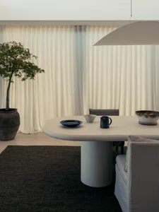 A modern minimalist living room featuring a concrete table and floor, with a potted tree in the corner and a large window wit
