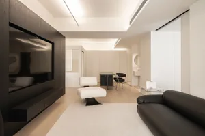 Modern, minimalist living room featuring white and neutral-toned decor with a wooden floor, white rug, black sofa, and white 