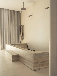 A minimalist marble bathroom with a large freestanding bathtub, modern fixtures, and a frosted glass shower door.