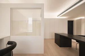 Modern minimalist office space featuring sleek white concrete walls and black furniture.