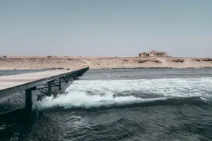 A wooden pier extending into the ocean with concrete structures in the background.