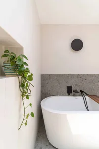 A minimalist bathroom with a white terrazzo bathtub and a green pothos plant.