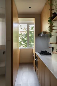 A minimalist kitchen with a white countertop and wooden cabinets, featuring a large window