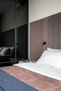 A neatly made bed with a textured cover and a white pillow, against a modern headboard with vertical lines.