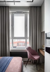 A modern bedroom featuring textured curtains and a cozy pink armchair.