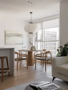 A modern minimalist living room with a round wooden table, chairs, and a pendant light hanging above. The room features a win