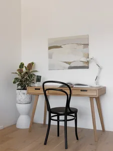 A modern work station featuring a wooden desk with a marble planter and a black chair, with a lamp and an abstract painting.