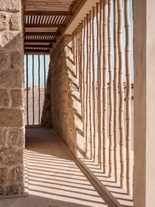 A corridor with stone walls and bamboo columns in the desert.